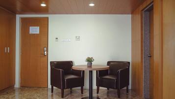 A lobby with a round table and two chairs, wooden doors, and a marble floor.