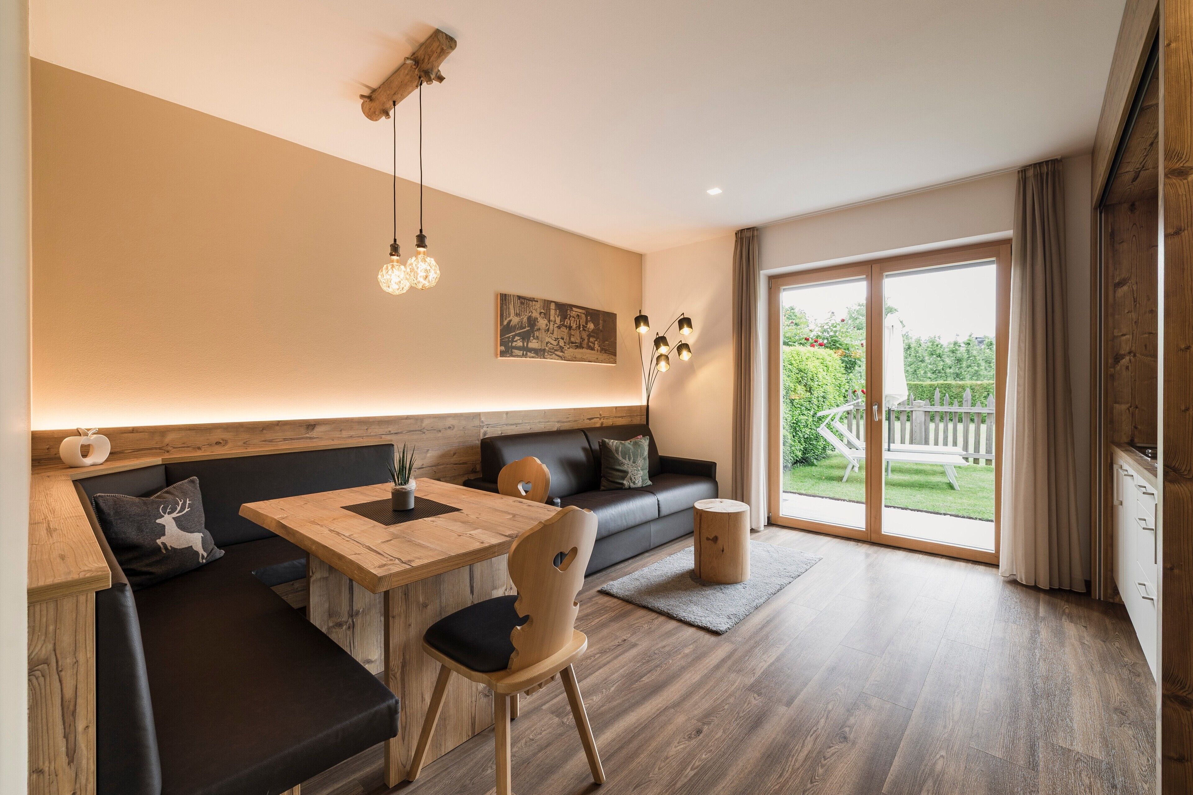 Un salon moderne avec une table à manger en bois, un canapé noir et une grande porte-fenêtre coulissante donnant sur un balcon.