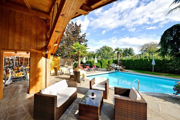 An outdoor pool area with wicker furniture, a covered seating area, and exercise equipment.
