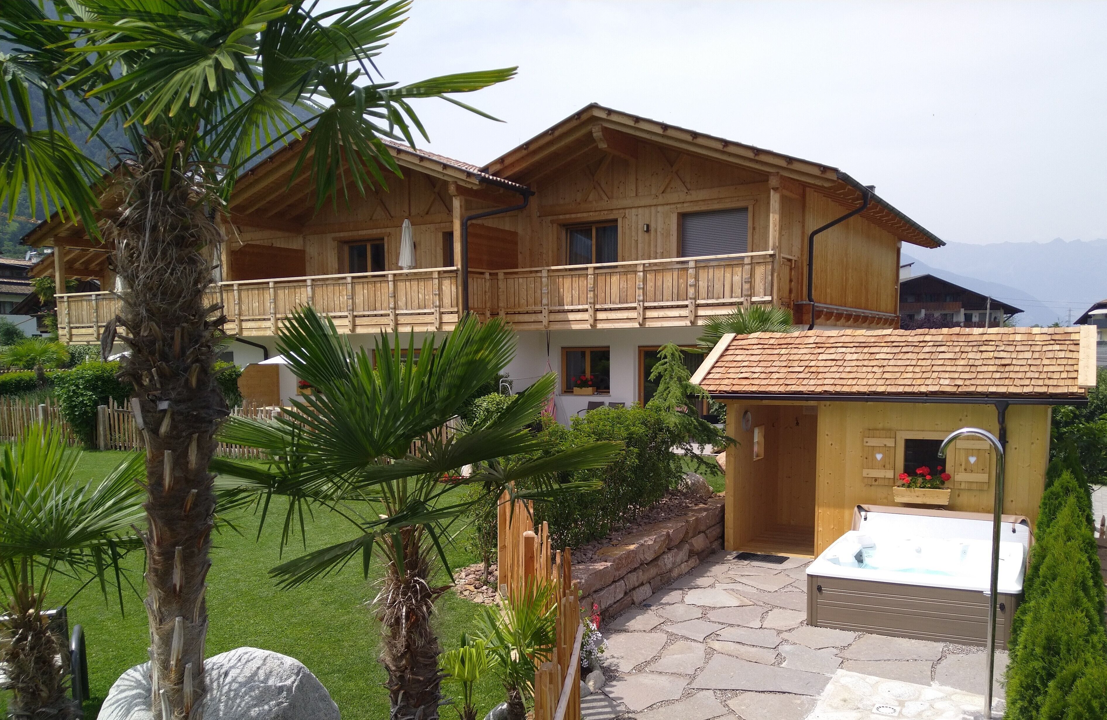 Un chalet en bois doté d’un balcon, d’un jacuzzi et d’un chemin bordé de pierres.