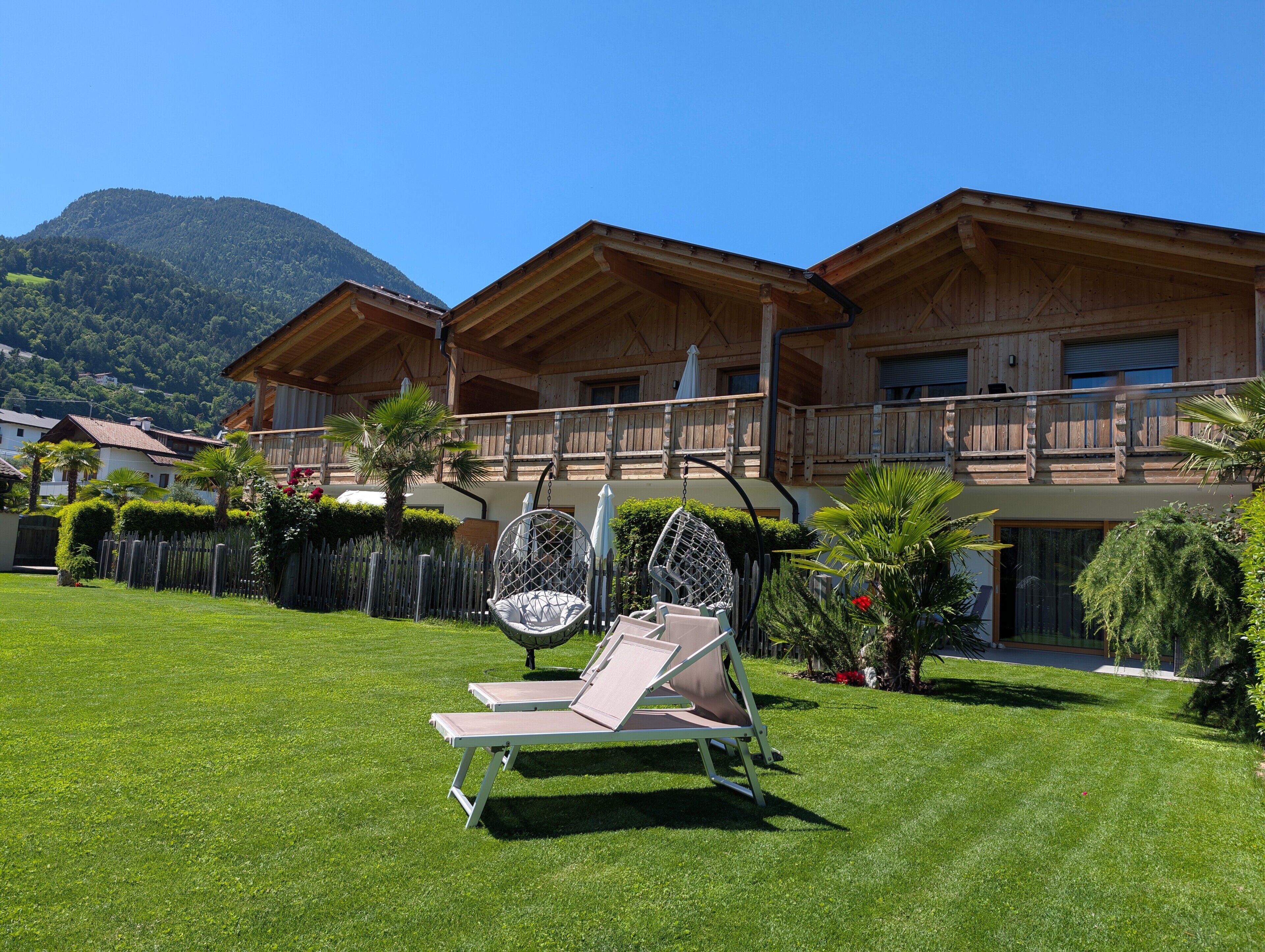 Eine Holzchalet mit Balkon, einem Hängesessel und einer Liege im Garten.