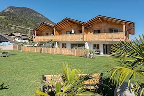 Un chalet en bois à deux étages, doté d’un balcon, entouré d’une pelouse bien entretenue et avec une vue sur les montagnes en toile de fond.