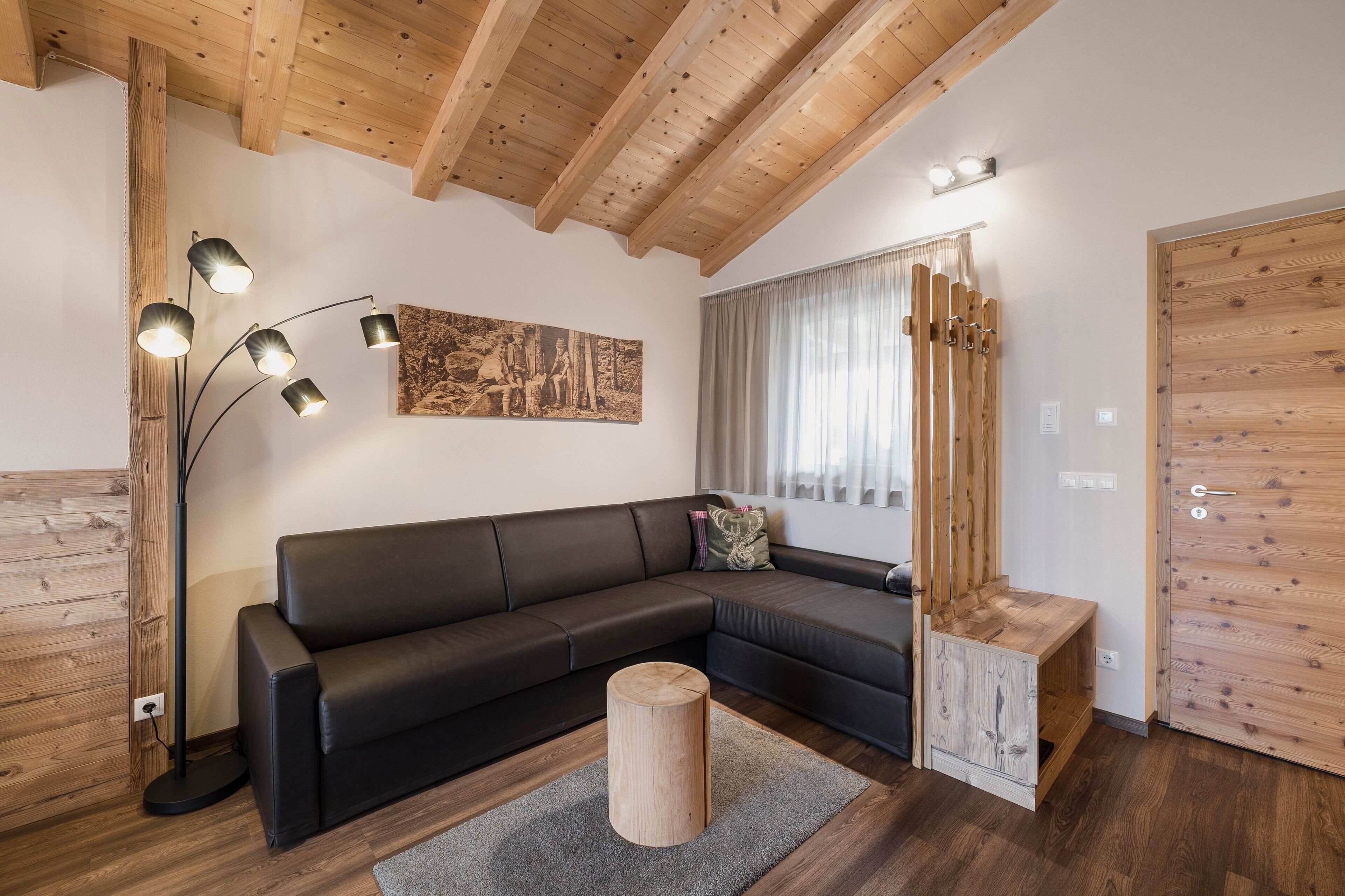 A modern living room with a sectional sofa, a wooden floor, a tall floor lamp, and a wooden door.