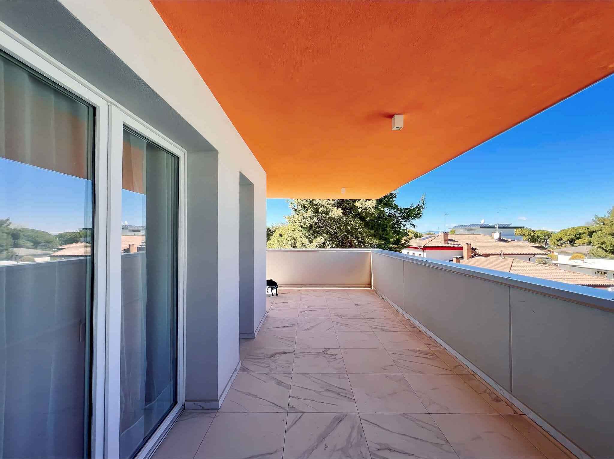 A balcony with a tiled floor, a glass door, and a clear view of the surrounding buildings and trees.