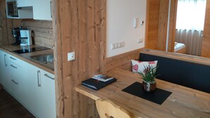 Une cuisine avec des meubles blancs, un mur en bois, une machine à café et une petite table sur laquelle se trouvent un livre et une plante.