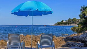 Two chairs and a blue umbrella on a stone pavement by the sea.