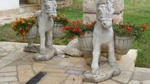 Two stone horse statues with flower pots on a stone-paved area.