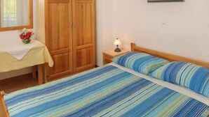 A room with a bed, a nightstand, a wooden wardrobe, a window with curtains, and a painting on the wall.