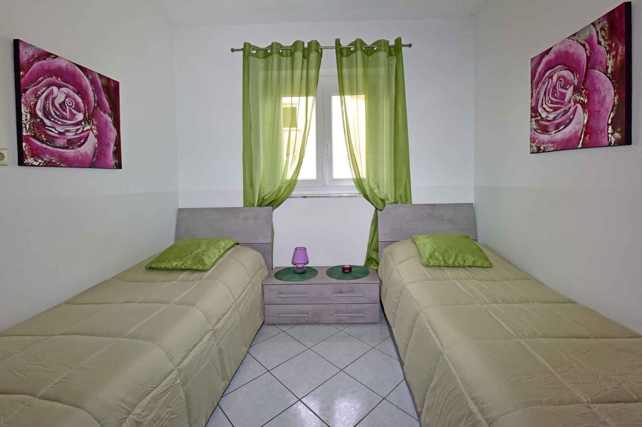 Una habitació amb dos llits, una finestra amb cortines verdes i dos quadres de roses a les parets.