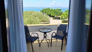 Een balkon met twee stoelen en een klein tafeltje, met uitzicht op een strand en groen.