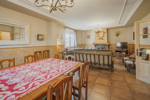 Un comedor con una mesa lista para cuatro, una cocina al fondo y un televisor sobre un soporte de madera.