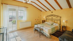 Une chambre à coucher comprenant un lit, un banc, une table de chevet avec une lampe, un radiateur et une fenêtre avec des rideaux.