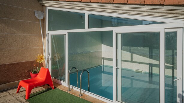 Une piscine avec des portes en verre, une chaise rouge et une plante en pot.