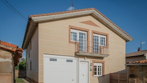 Un immeuble de deux étages avec une porte de garage blanche, un balcon doté d’une rambarde en métal et une petite fenêtre à l’étage supérieur.