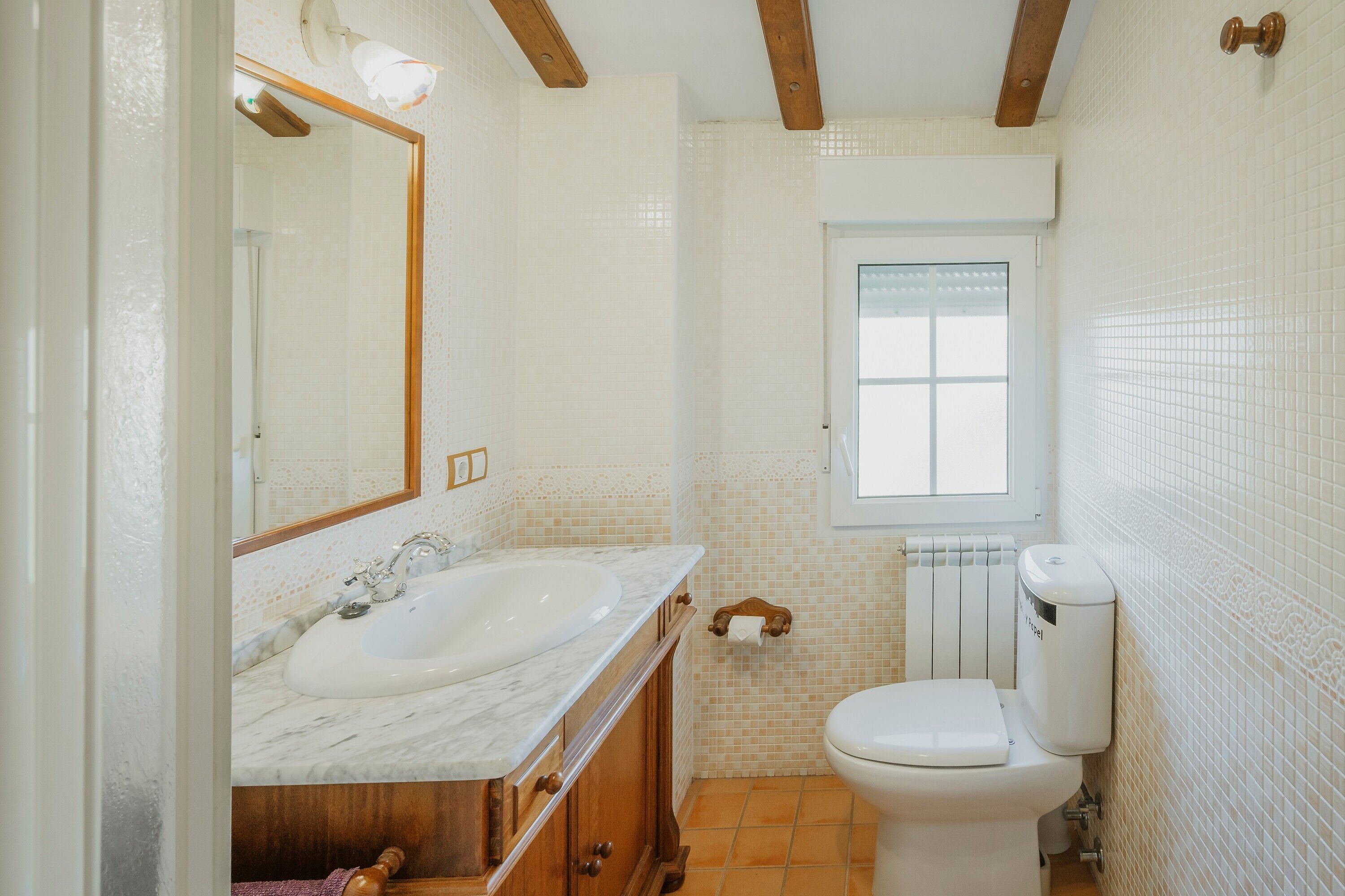 A bathroom with a sink, mirror, toilet, and window.