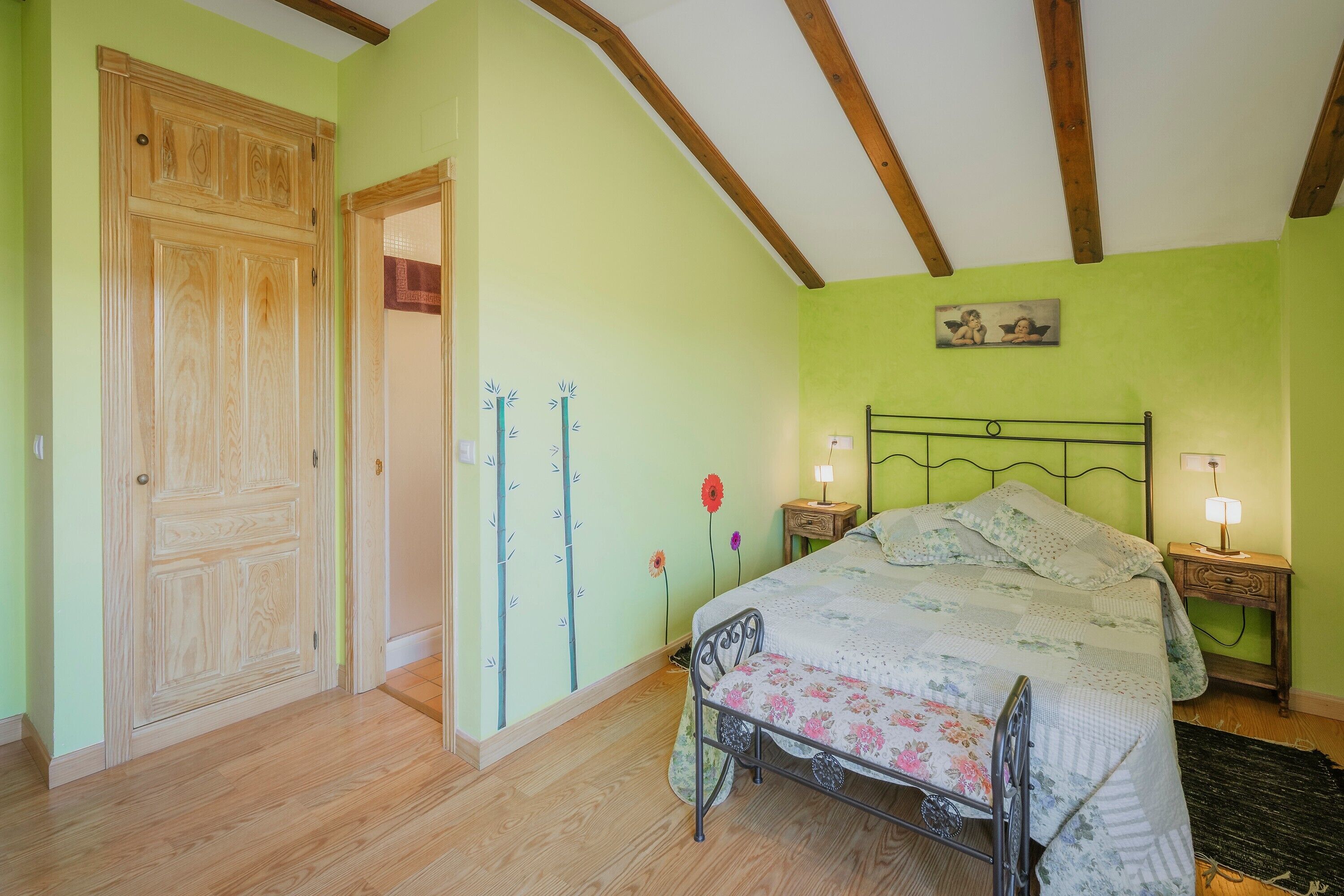 Un dormitorio con cama, puerta de madera y mesita de noche con lámpara.