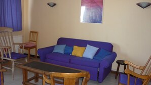 Ein Wohnzimmer mit einem violetten Sofa, Holzstühlen, einem Couchtisch und einem Poster an der Wand.