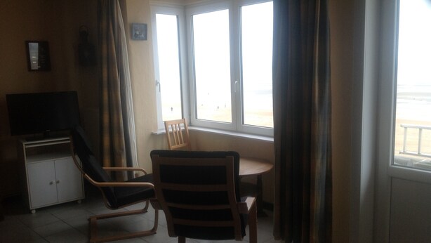 Ein Zimmer mit Schreibtisch, zwei Stühlen, einem Fernseher und einem fenster mit Vorhängen.