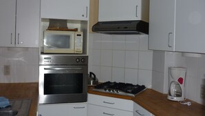 Eine Küche mit weißen Schränken, einer Mikrowelle, einem Backofen, einem Gasherd und einer Kaffeemaschine.