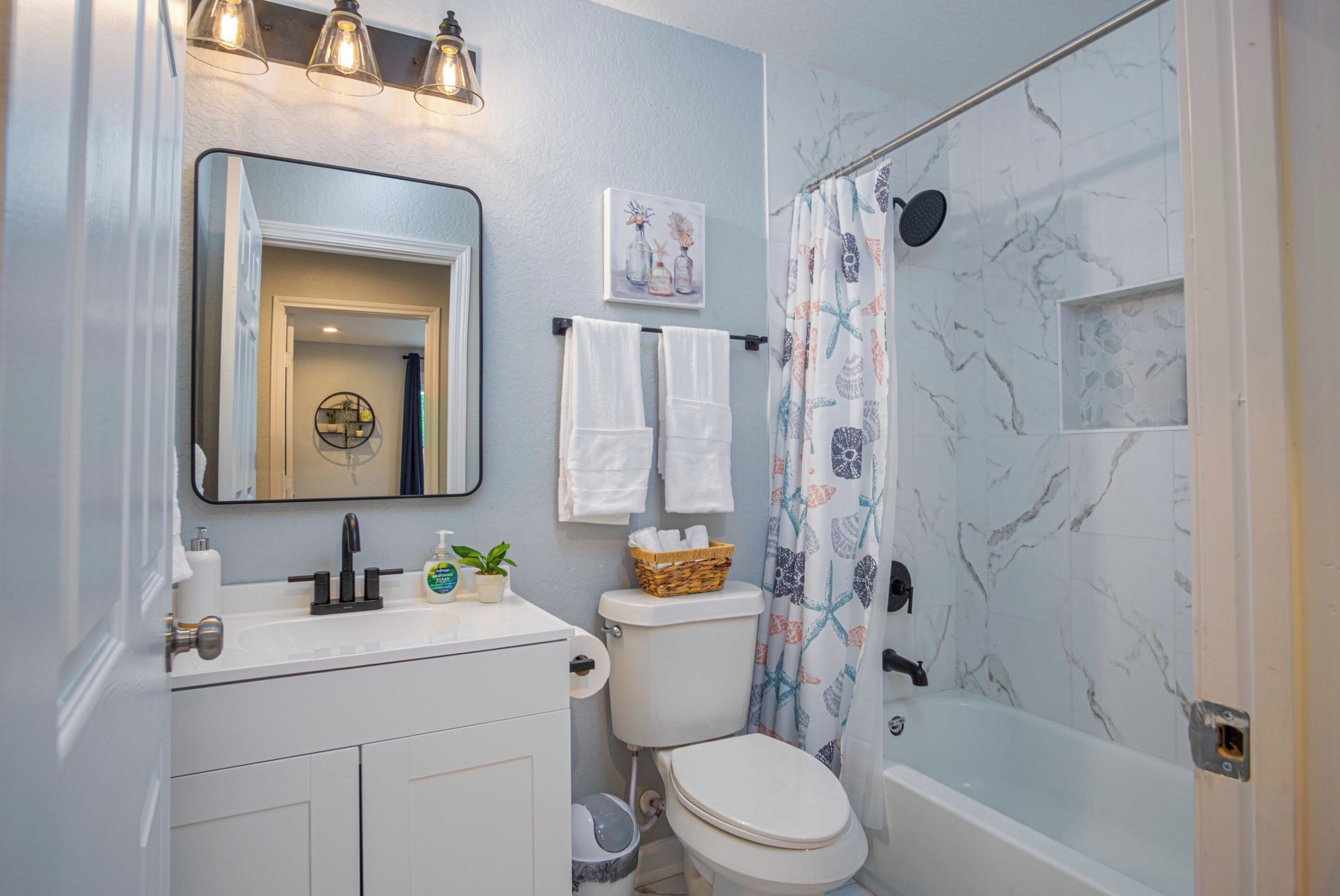 A bathroom with a white sink, mirror, and toilet. There is a shower curtain with a floral pattern and a bathtub.