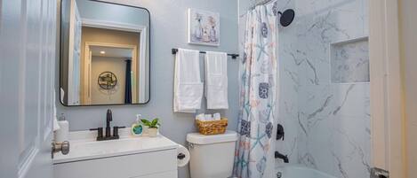 A bathroom with a white sink, mirror, and toilet. There is a shower curtain with a floral pattern and a bathtub.