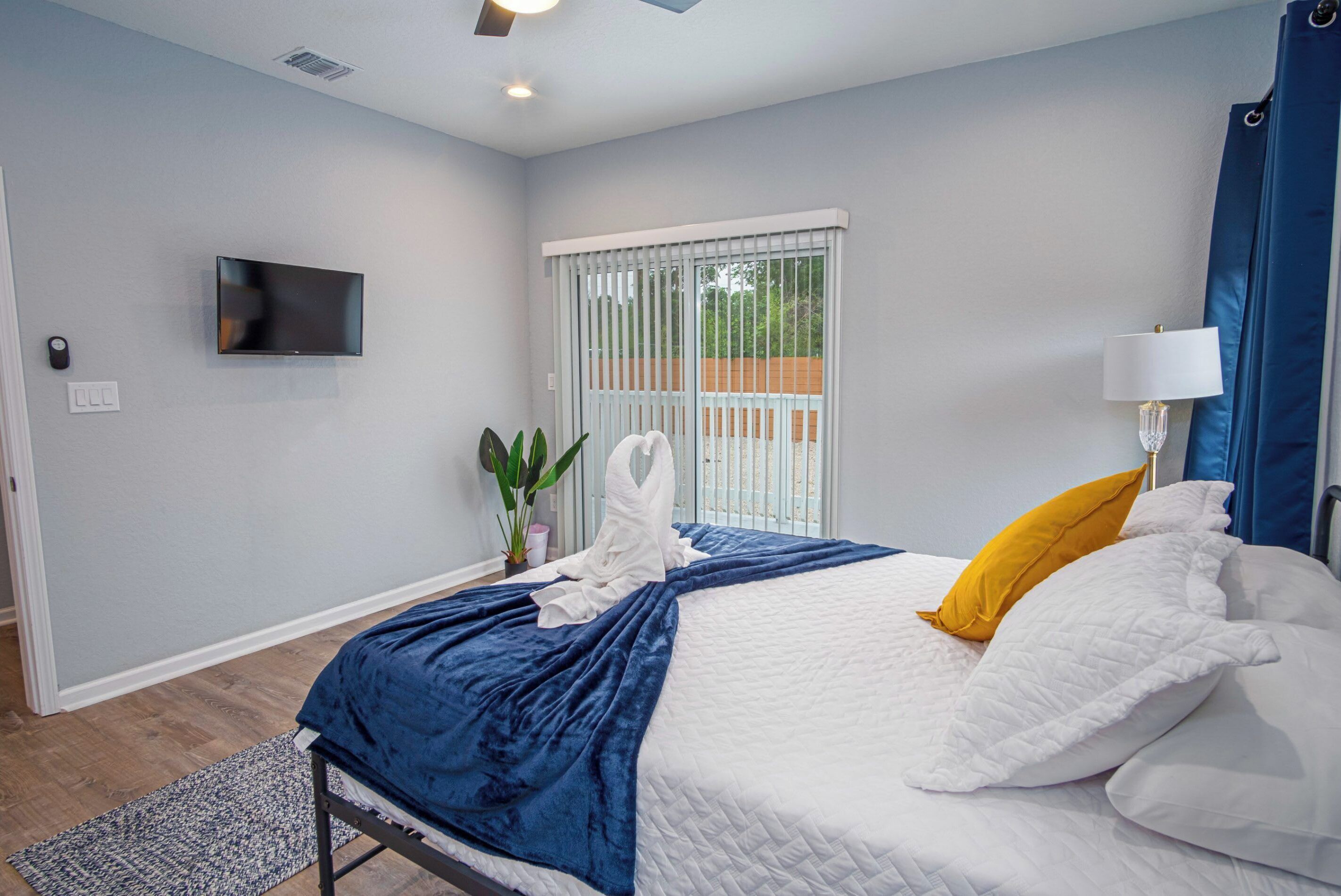 Un dormitorio moderno con cama, televisor, ventana con persianas y una planta.