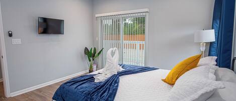Un dormitorio moderno con cama, televisor, ventana con persianas y una planta.