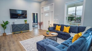 Un salon moderne avec un canapé d’angle, une table basse et un téléviseur à écran plat fixé au mur.