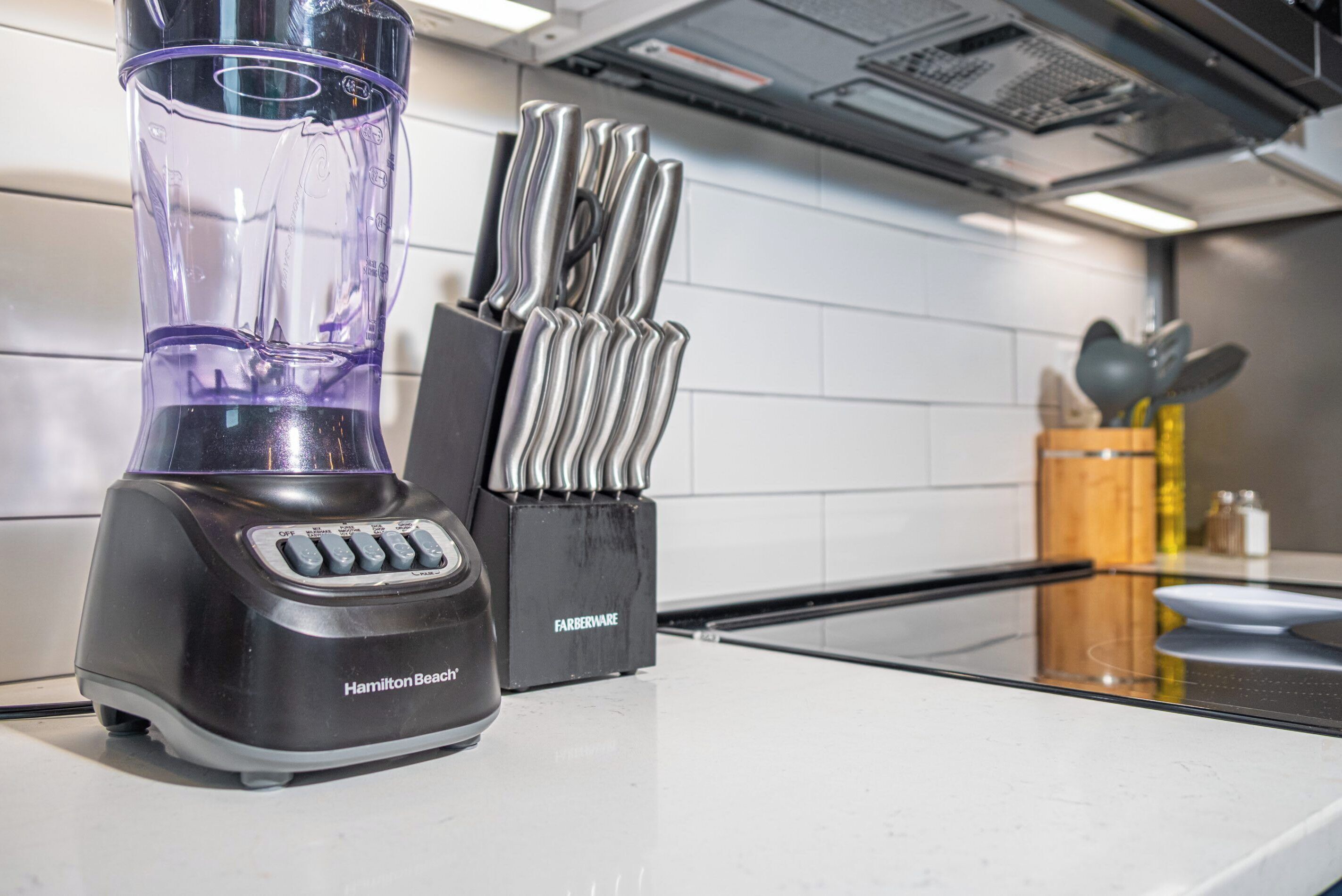 A kitchen with a Hamilton Beach blender, a knife block, and a stovetop.