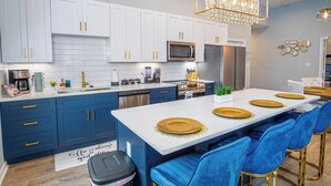 Une cuisine moderne avec des meubles blancs, un îlot central agrémenté de touches dorées et un lustre.