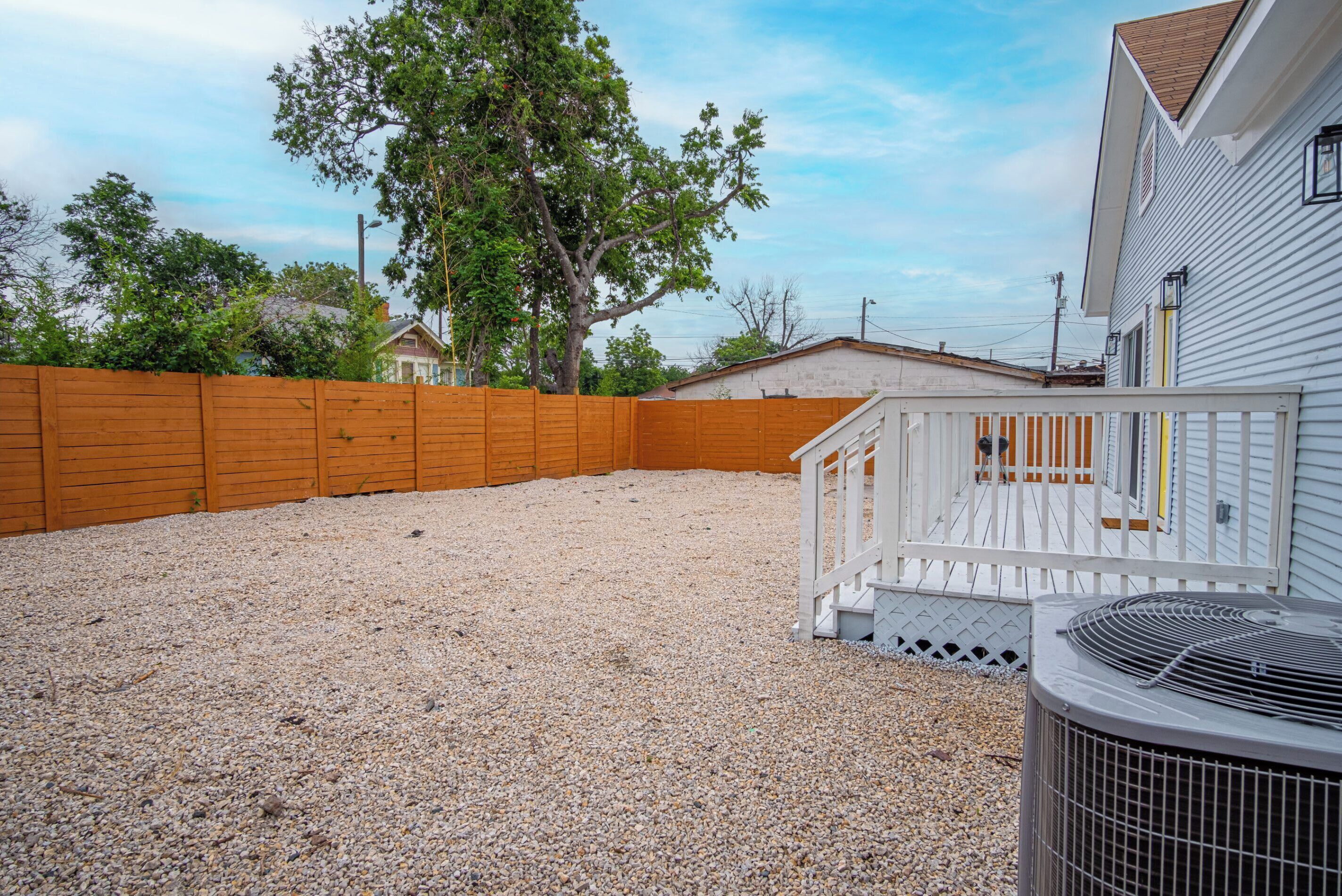 A backyard with a wooden fence, gravel ground, and a white building with a porch.