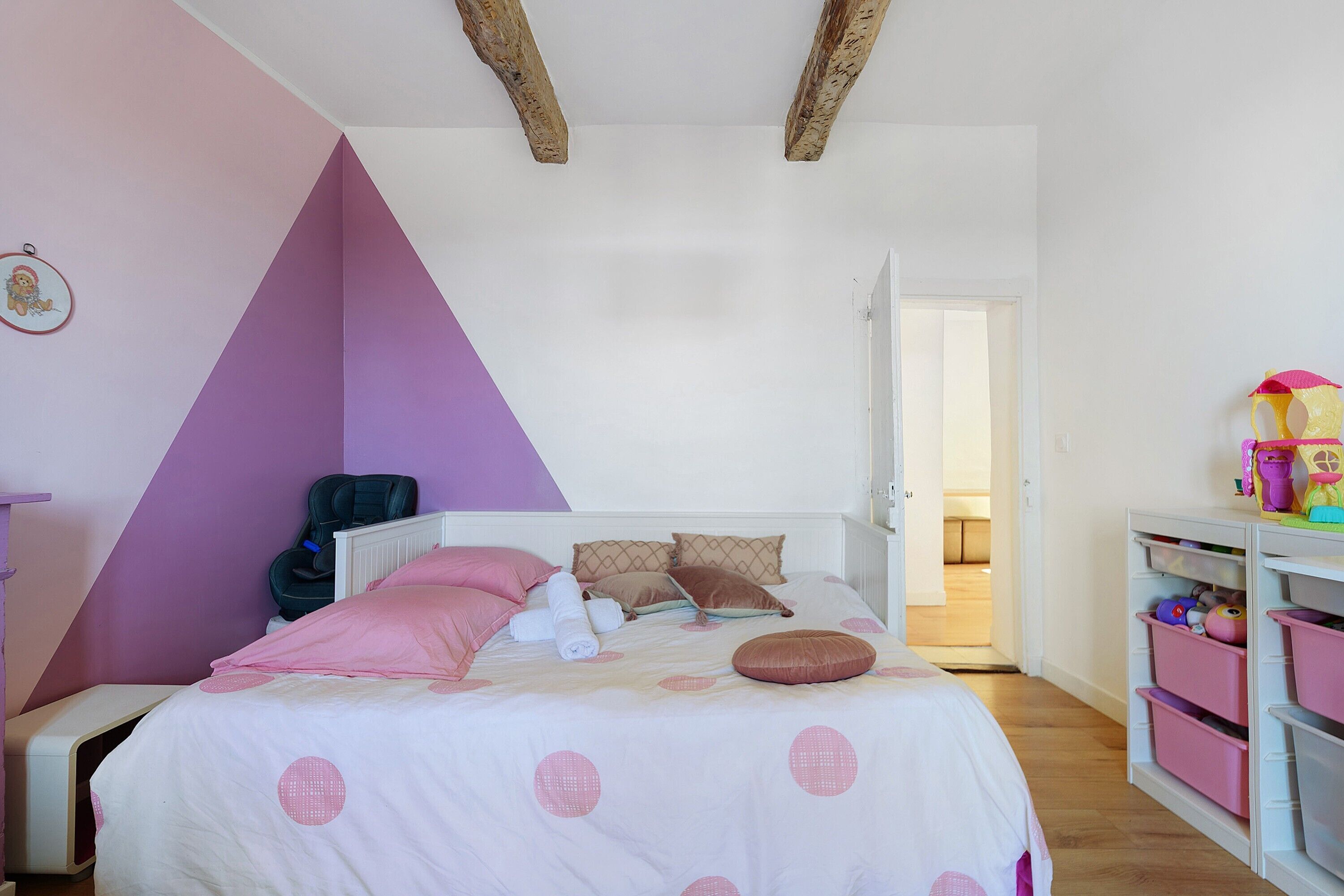 Un dormitorio con cama, almohadas, un radiador, una puerta y un mueble para guardar juguetes.