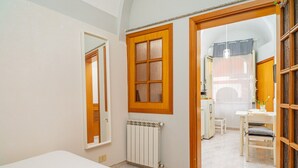 A room with a bed, a radiator, a wooden door, and a view into a dining area.