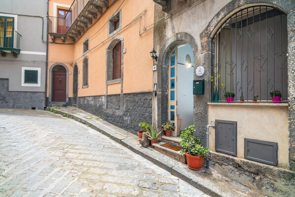 Une rue pavée, un immeuble avec une porte en bois et des plantes en pot sur le trottoir.