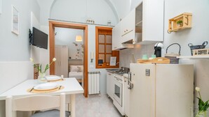 Een compacte keuken met witte kastjes, een eettafel met placemat, een koelkast en een koffiehoek.