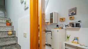 A kitchen with a refrigerator, coffee machine, and a wooden shelf with books and a vase.