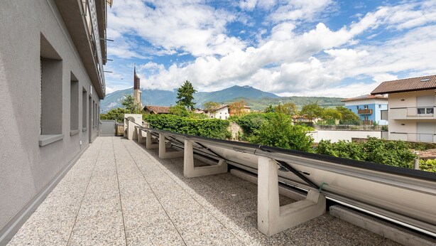 A balcony with a view of a mountain, buildings, and greenery.