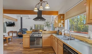 A modern kitchen with wooden cabinets, a stainless steel stove, and a large window offering a view of trees.