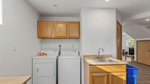 A kitchen with two white washing machines, wooden cabinets, a sink, and a countertop. - Sterling Hideout on the Kenai Peninsula (Sterling)