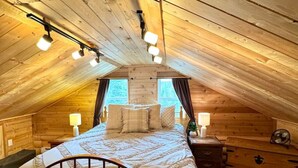 A cozy attic bedroom with a wooden sloped ceiling, a metal bed frame, and a nightstand with a lamp.