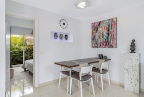 A modern dining area with a wooden table, white chairs, a clock, and a colorful abstract painting.