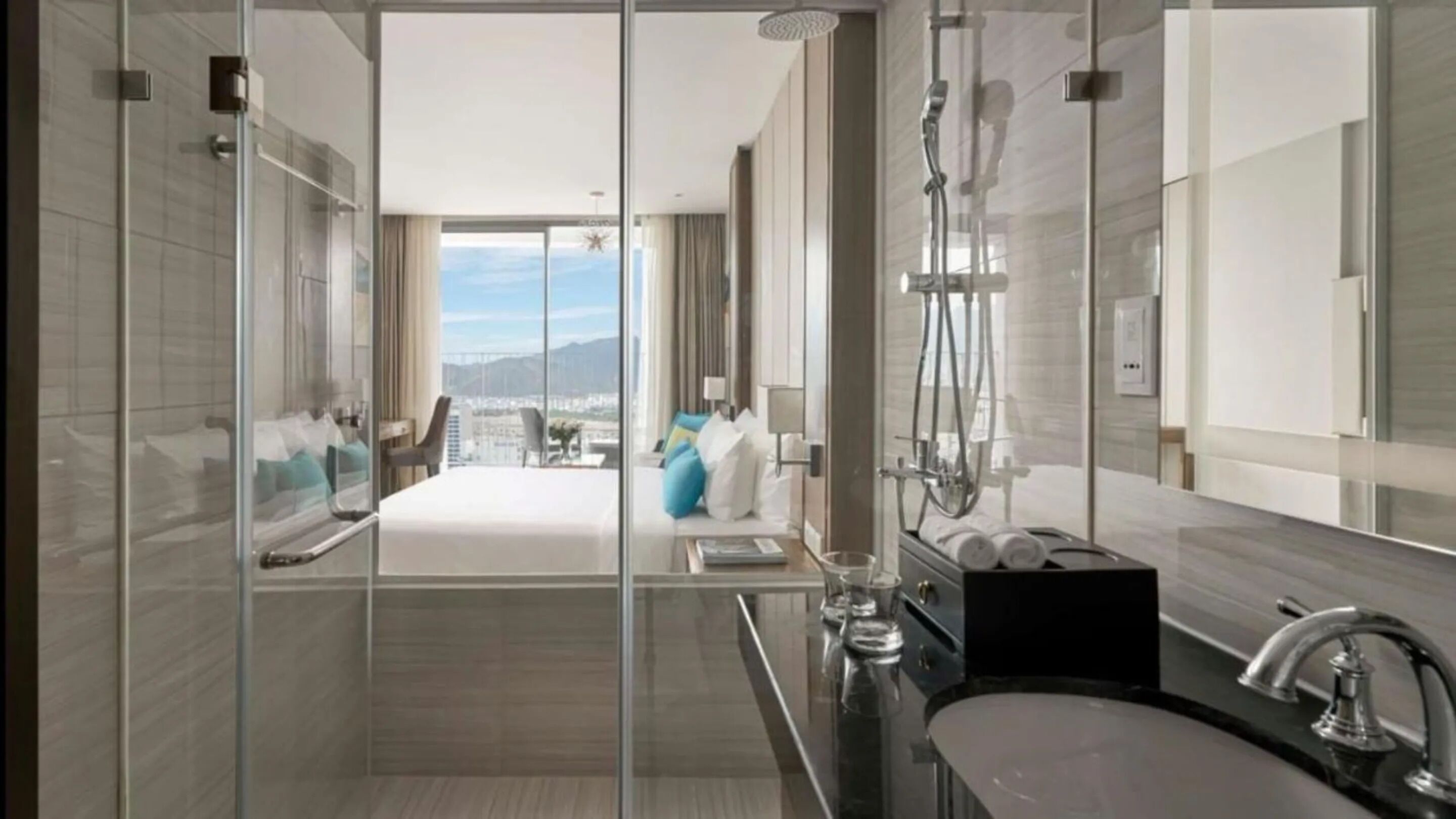 A modern bathroom with a glass shower enclosure, a large mirror, and a view of a bedroom with a balcony.