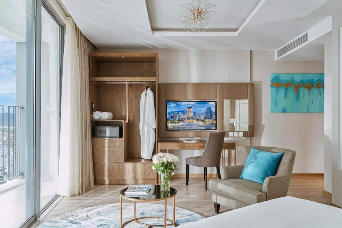Een moderne hotelkamer met een groot raam, een flatscreen televisie, een bank, een stoel en een houten garderobe.
