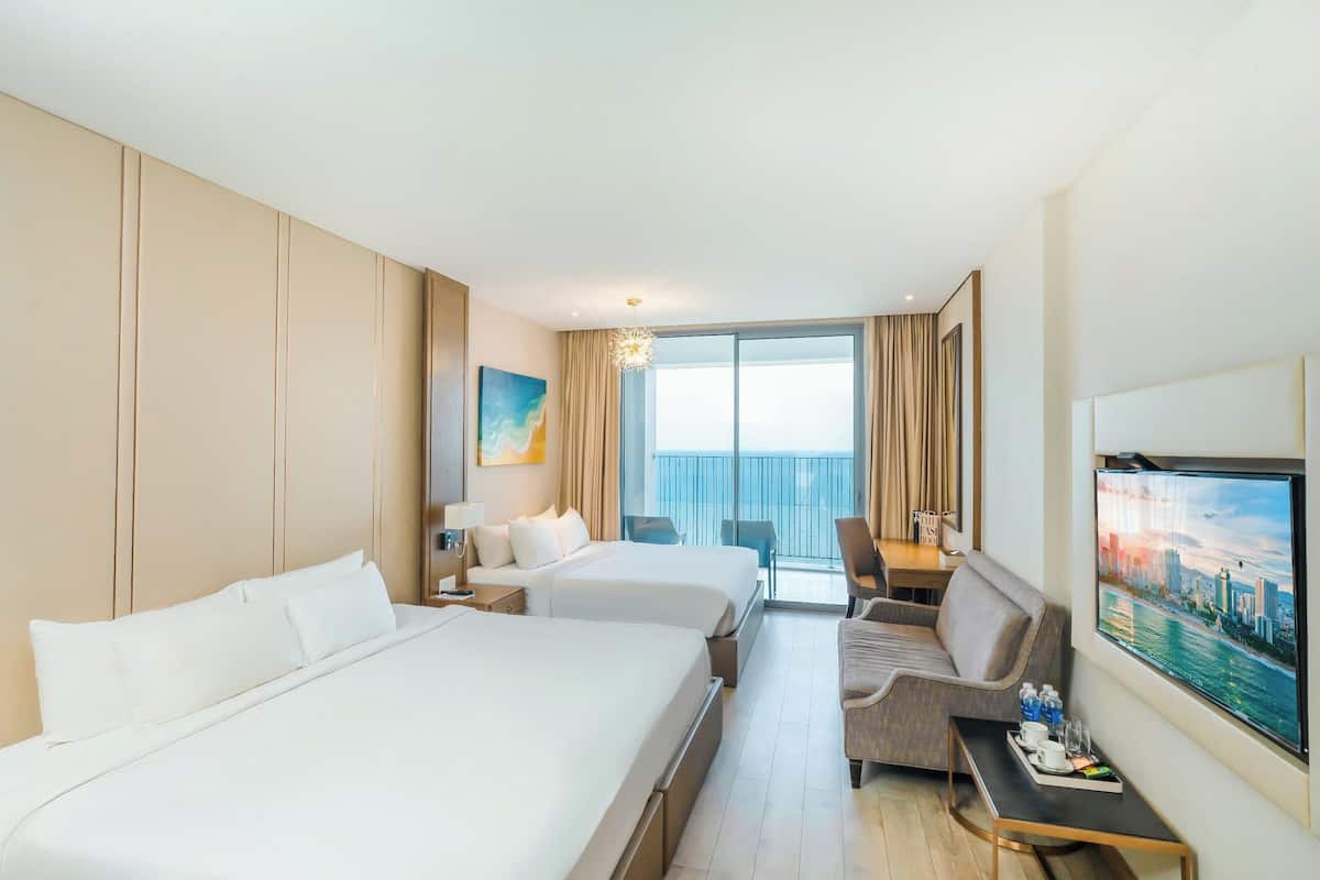 Een hotelkamer met twee bedden, een bureau, een stoel, een televisie en een balkon met gordijnen.