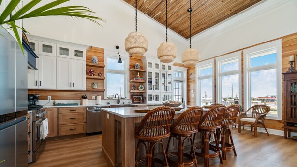 A spacious kitchen with wooden cabinets, a large island, and wicker chairs. - Sea Salt Cottage with private boat dock (Atlantic Beach)