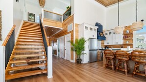 A spacious kitchen with a wooden staircase, white cabinets, and a dining area with wicker chairs. - Sea Salt Cottage with private boat dock (Atlantic Beach)