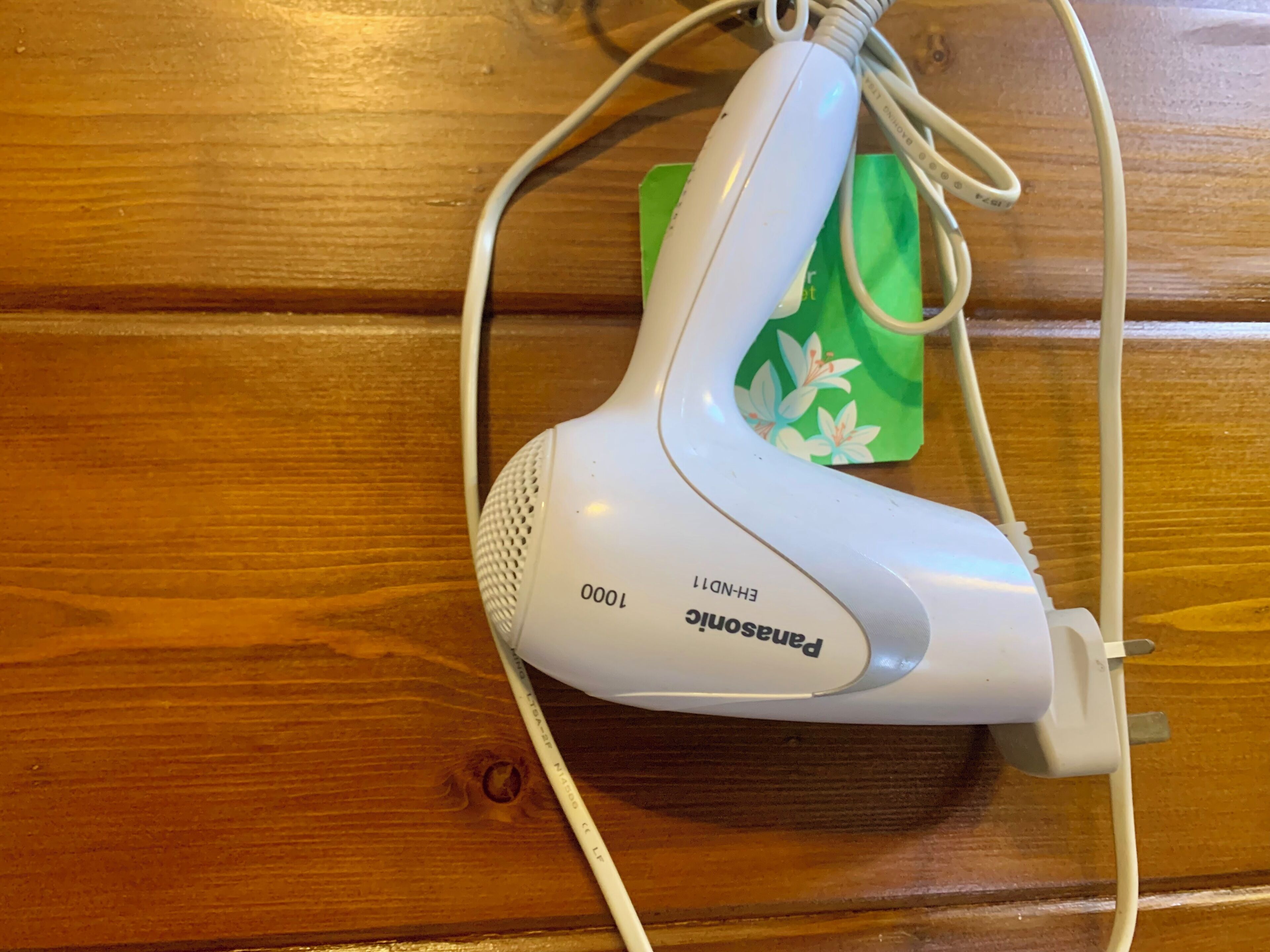 Un secador de pelo Panasonic sobre una superficie de madera, con un objeto verde al fondo.