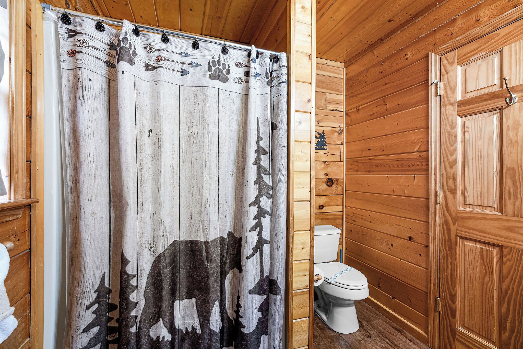 Bagno di una baita in legno con tenda da doccia a fantasia animalier, un water e pareti in legno.