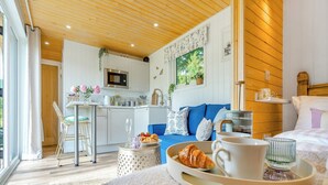 A cozy room with a bed, a dining area with a table and chairs, a kitchen with a microwave, and a large window. - Freedom Fields - Bluebell (Straiton, near Maybole)