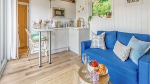 A modern kitchen with white cabinets, a wooden ceiling, and a dining area with a blue sofa and a table with food and drinks. - Freedom Fields - Bluebell (Straiton, near Maybole)